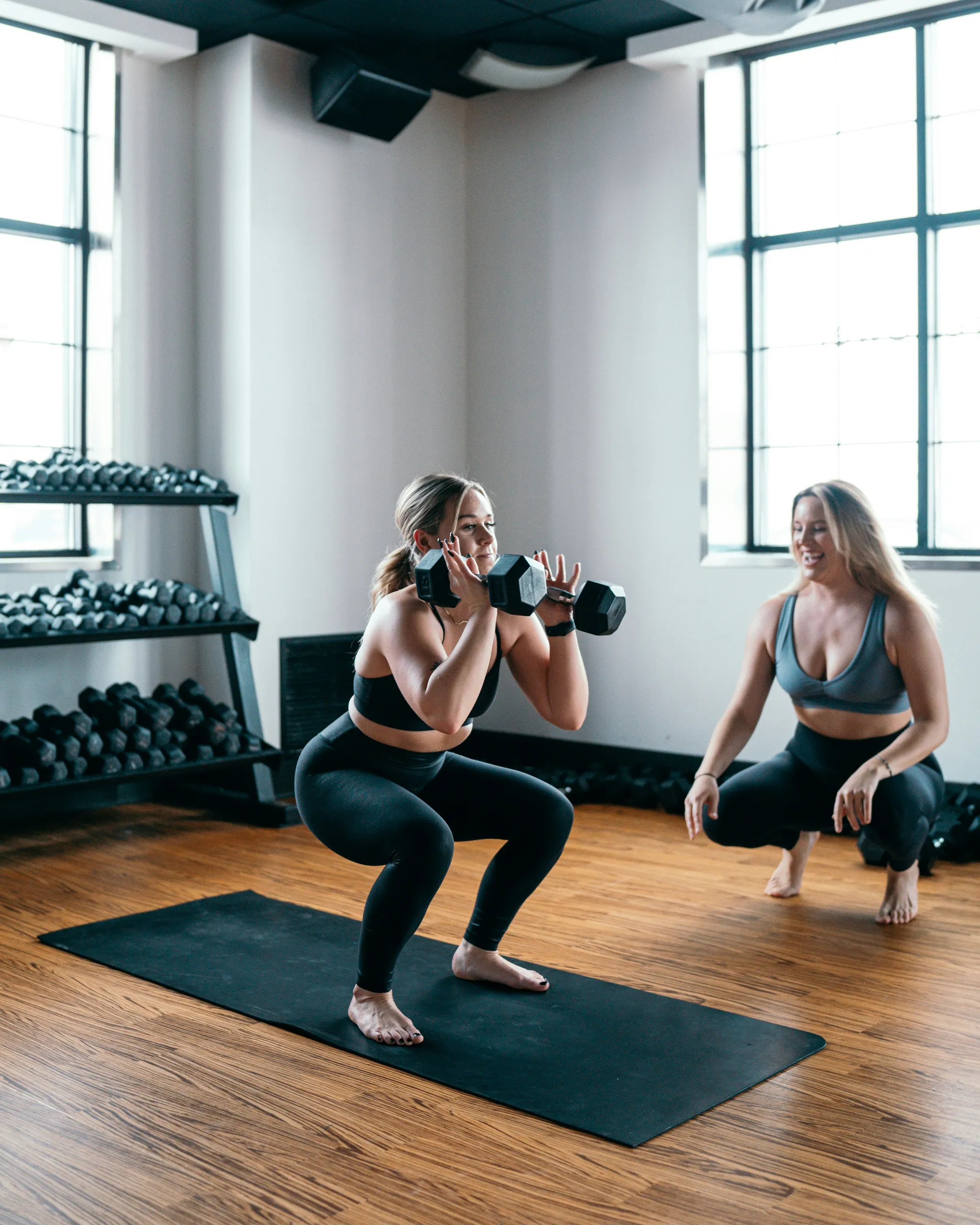 Entrenamiento personal: dos mujeres hacen sentadillas con mancuernas en el estudio